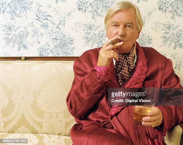 senior man sitting on sofa, smoking cigar and holding glass, portrait - ascot foto e immagini stock