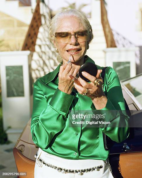senior woman standing by car, applying make-up, close-up - groen shirt stockfoto's en -beelden