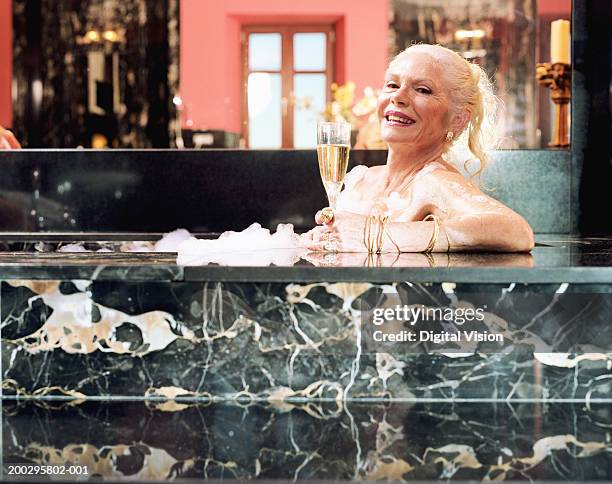 mature woman relaxing in hot tub, holding champagne flute, portrait - senioren in bad stock-fotos und bilder