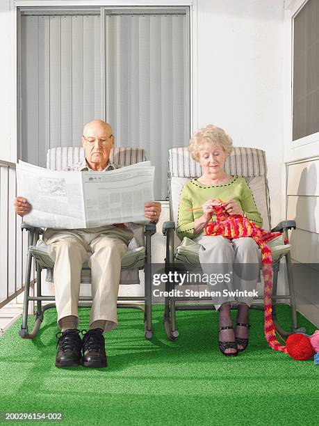 senior couple sitting on patio, man reading paper, woman knitting - man knitting stock pictures, royalty-free photos & images
