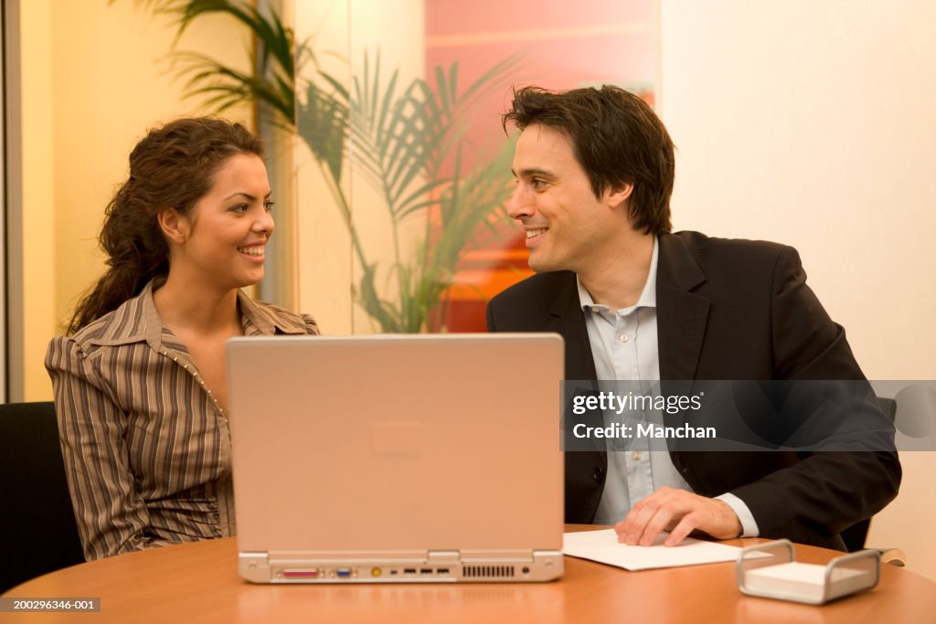 Businessman and businesswoman sitting at laptop in meeting, smiling