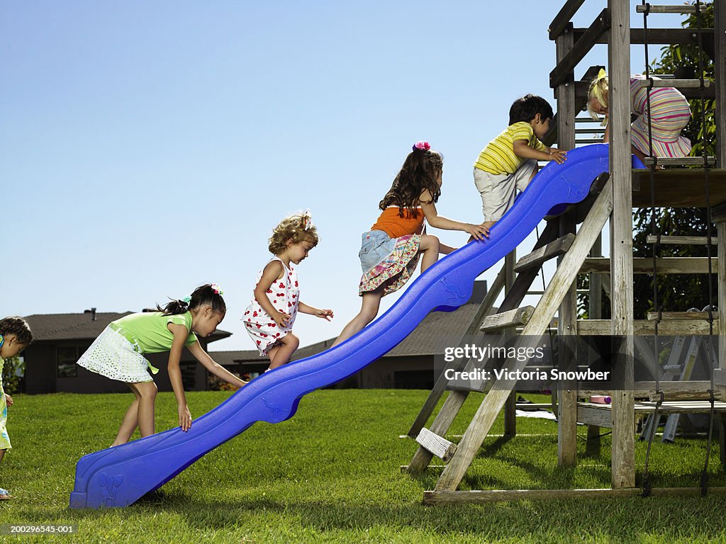 Children (4-6) climbing up slide in playground