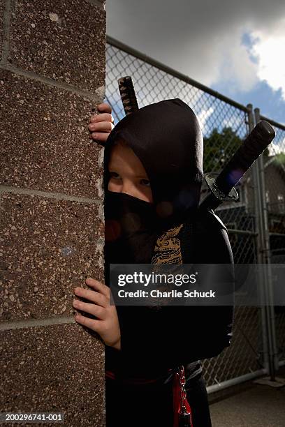 boy (9-11) in ninja costume, looking around corner of building - ninja kid stock-fotos und bilder