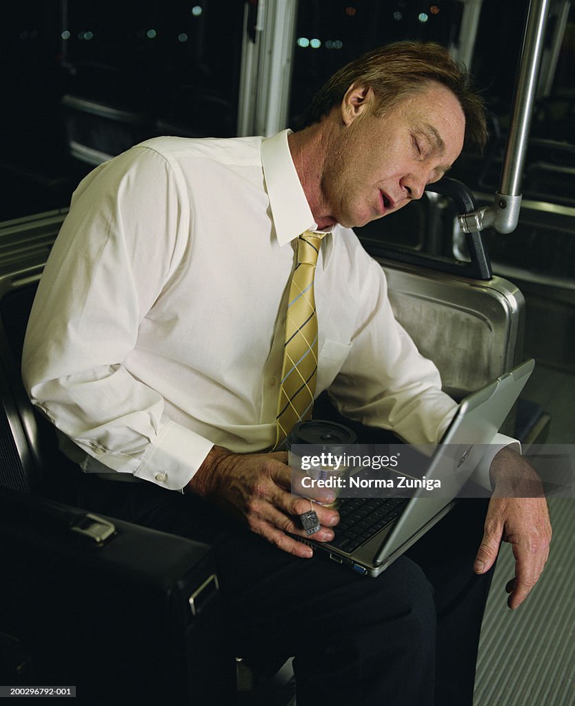 Mature businessman with laptop computer sleeping on bus