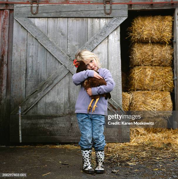 girl (5-7) hugging chicken outside barn, portrait - hugging animals foto e immagini stock