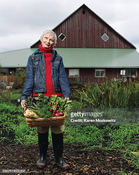 senior woman holding basket of produce on farm, portrait - kohlrübe stock-fotos und bilder