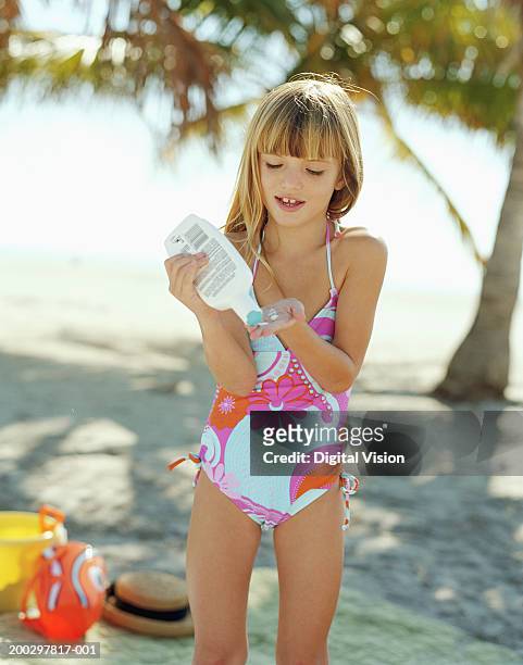 girl (6-8) on beach squeezing sun cream into palm of hand, smiling - young girl swimsuit stockfoto's en -beelden