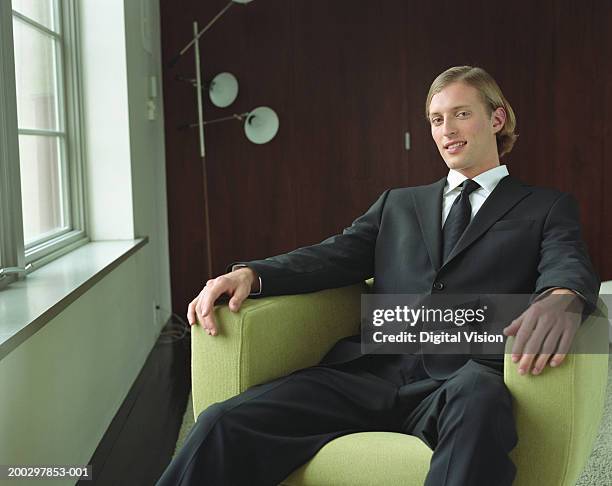 young businessman sitting in armchair, smiling, portrait - selbstzufrieden stock-fotos und bilder