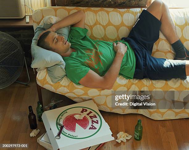 man lying on sofa, discarded take-away boxes and beer bottles on floor - gestalt stock-fotos und bilder