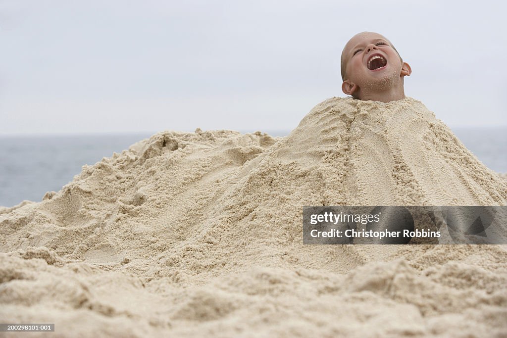 Boy (2-4) buried in mound of sand, shouting (Digital Composite)