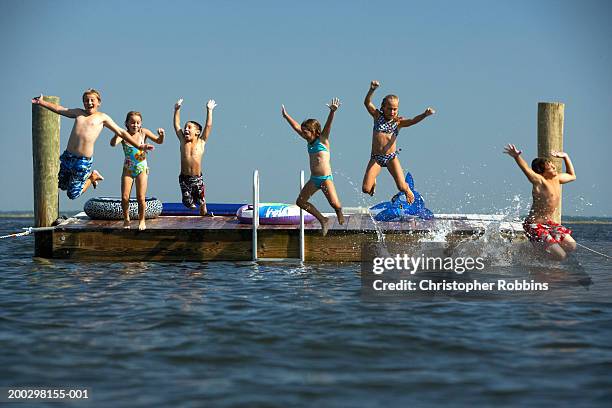 group of children (5-12) leaping off landing platform into sea - floating platform stock pictures, royalty-free photos & images