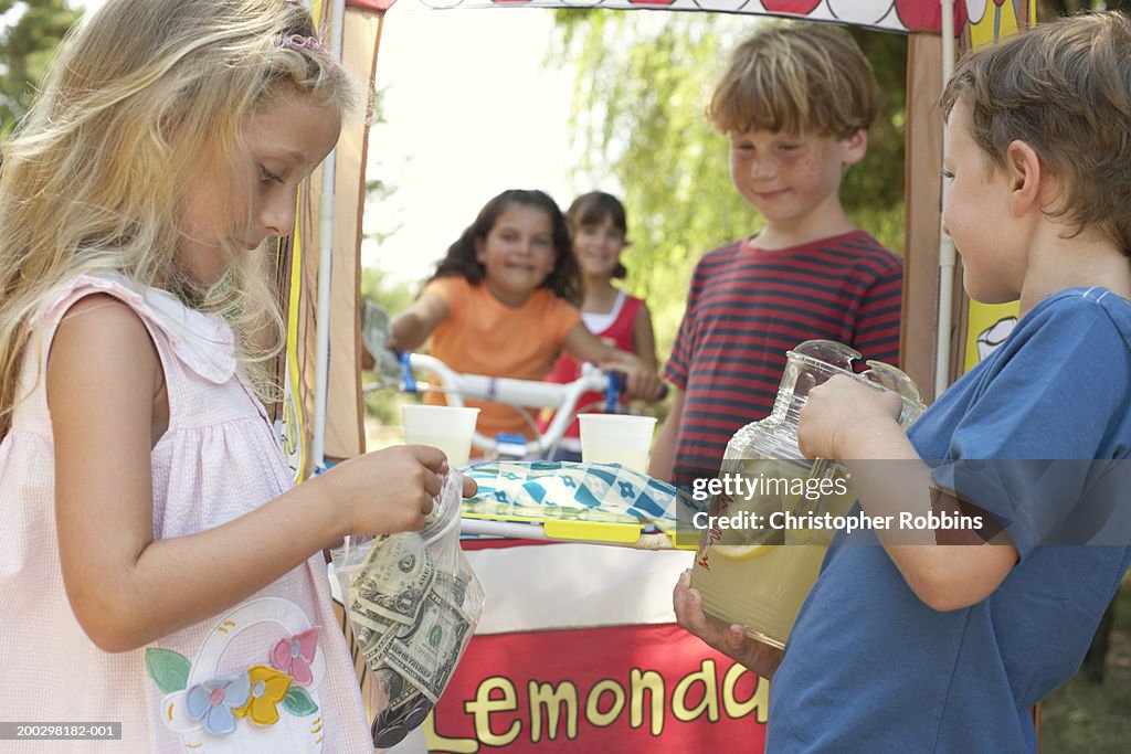 Children (6-12) at lemonade stall, girl (5-7) putting money in bag