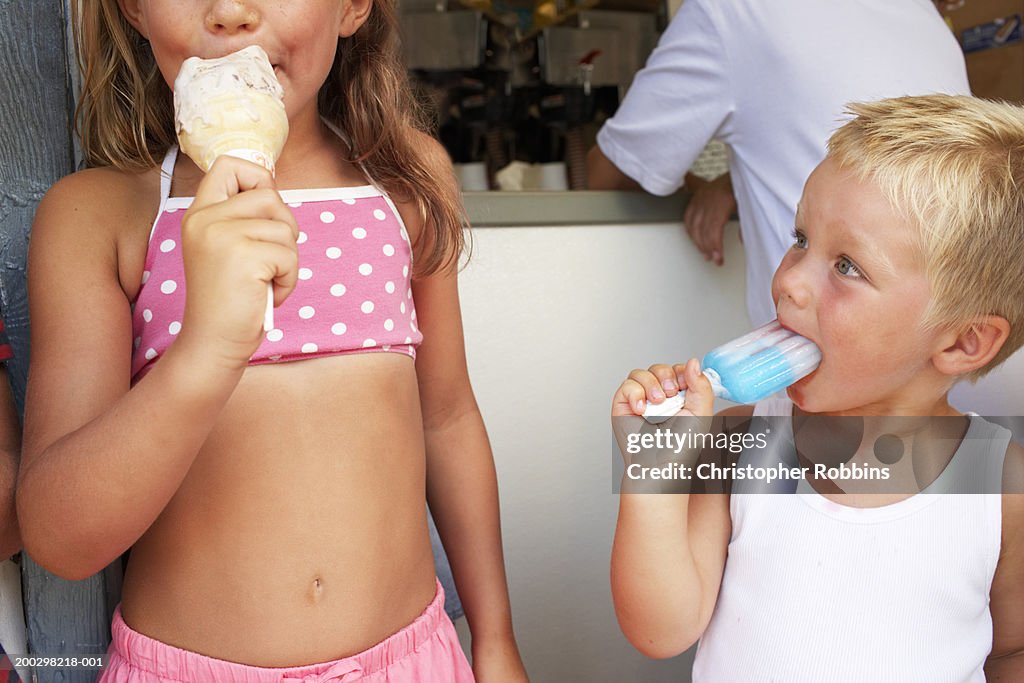 Girl (6-8) and boy (2-4) eating iced treats by tuck shop, close-up