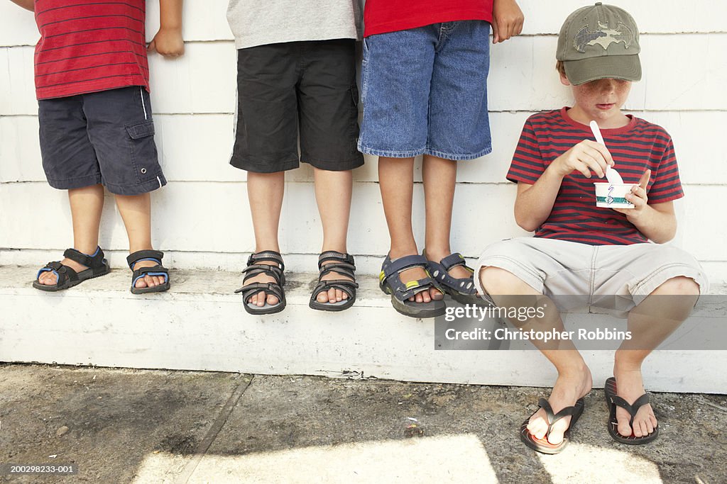 Four boys (4-9) eating ice cream by wall, one sitting