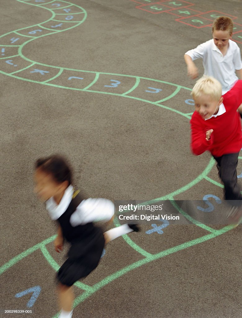 Three children (6-8) running in playground (blurred motion)