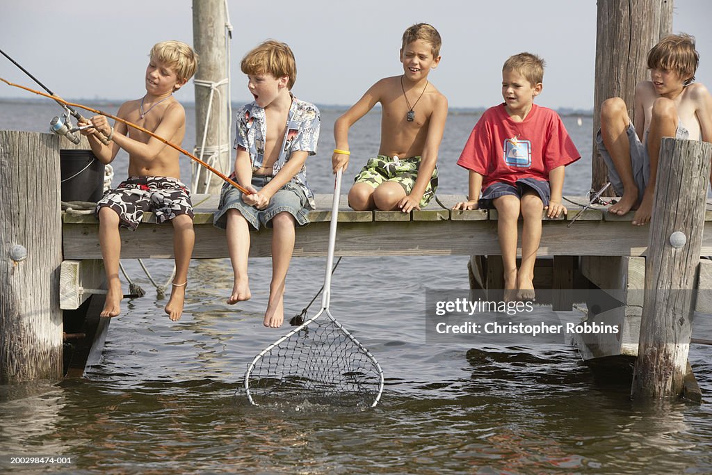 Five boys (5-13) sitting on jetty fishing, one holding net in water