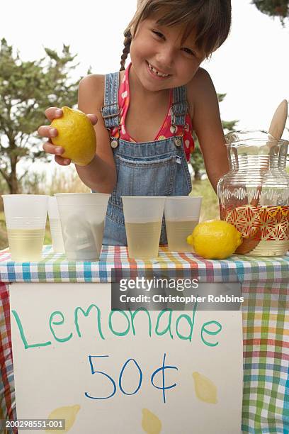 girl (5-7) tending lemonade stall, holding lemon, smiling, portrait - buvette photos et images de collection