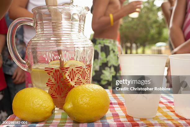 jug, lemons and cups on lemonade stall, children (5-13) in background - レモネード売り ストックフォトと画像