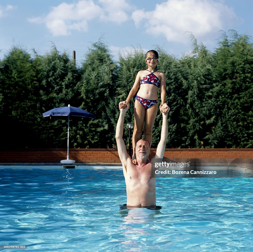 Girl (7-9) standing on grandfather's shoulders in swimming pool