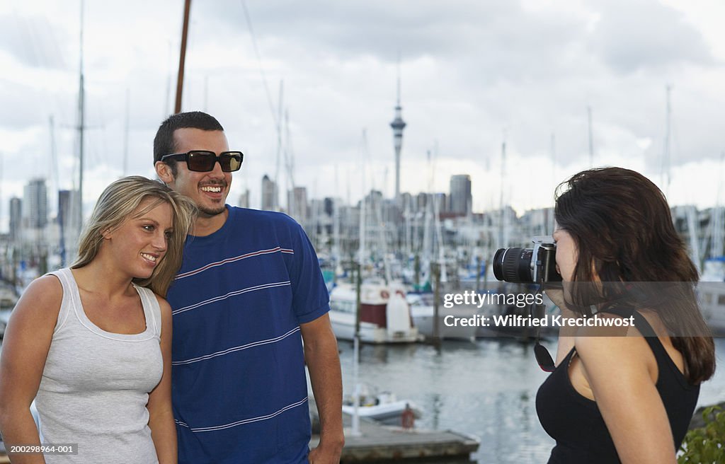 Young woman photographing couple in marina, smiling