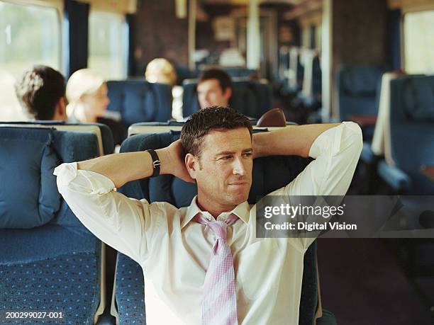 businessman relaxing on train, hands behind head (focus on man) - 通勤電車 ストックフォトと画像