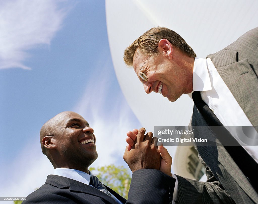 Two businessmen greeting each other in street, smiling, low angle view