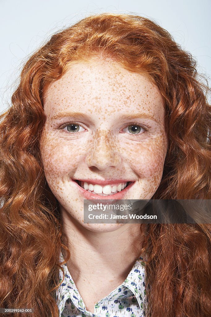 Teenage girl (13-15) with curly hair and freckles, smiling, portrait