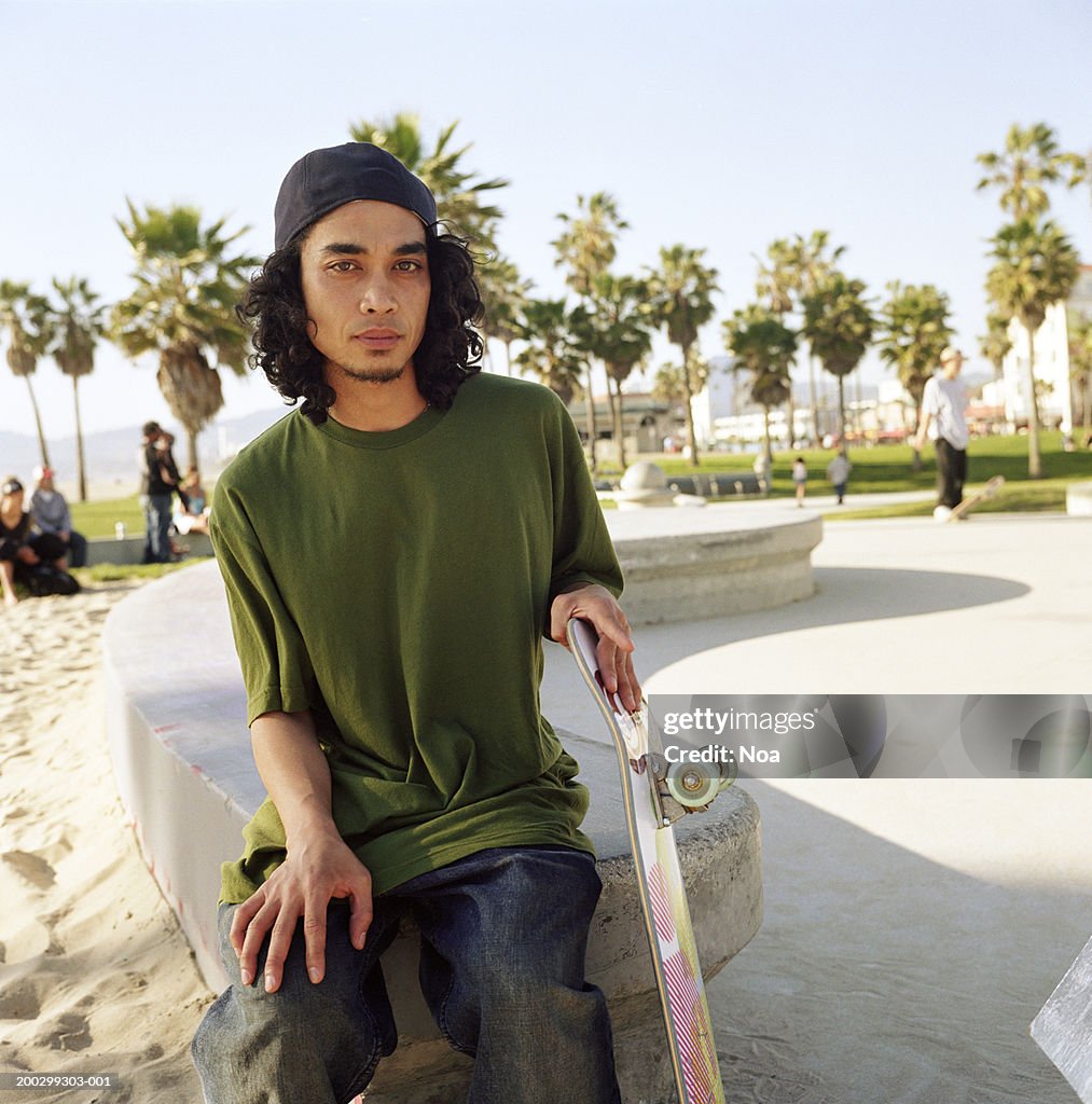 Man sitting on wall holding skateboard, portrait