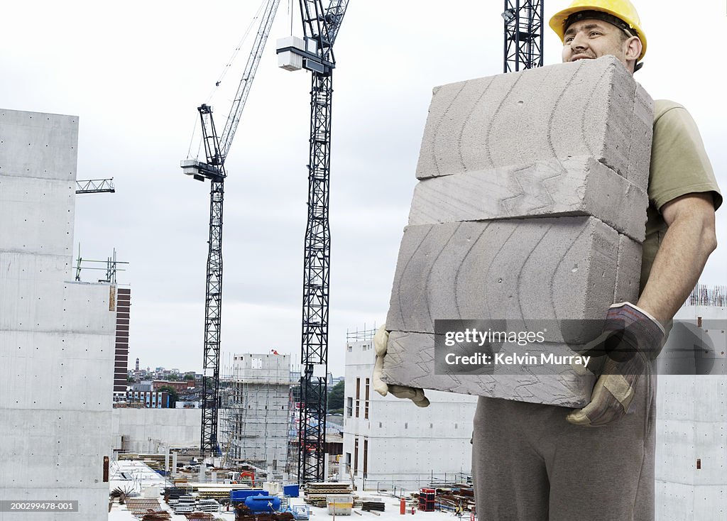 Construction worker carrying breeze blocks on building site, smiling