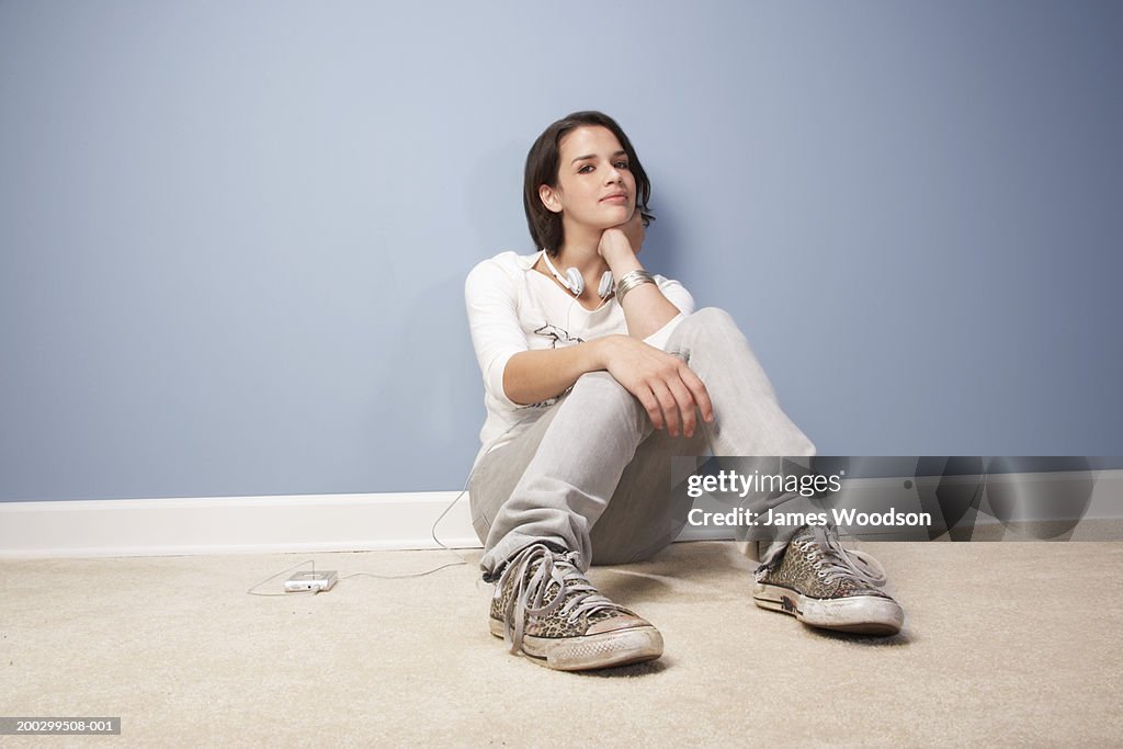 Teenage girl (16-18) sitting against wall, smiling, portrait