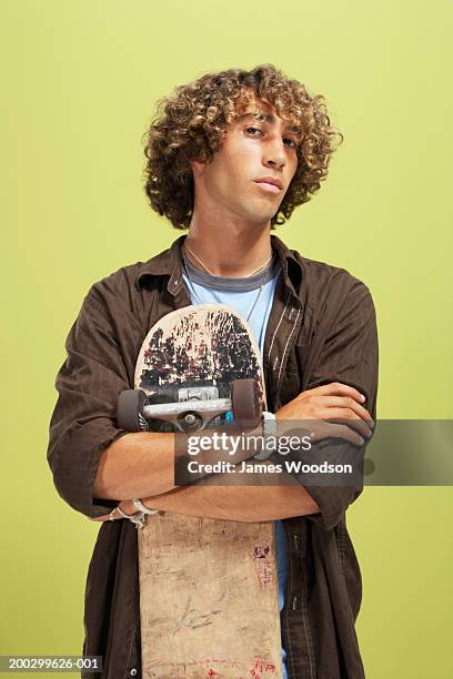 teenage boy (16-18) with curly hair, holding skateboard, portrait - skater boy hair stock pictures, royalty-free photos & images