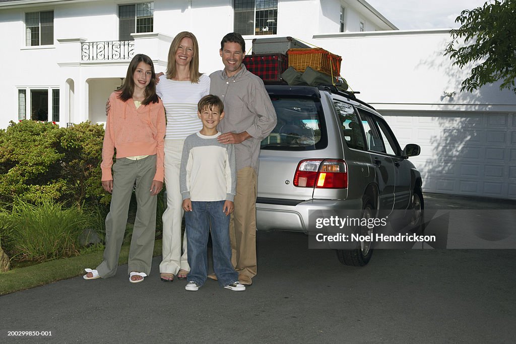 Couple standing with son and daughter (8-13 years) beside car in front drive