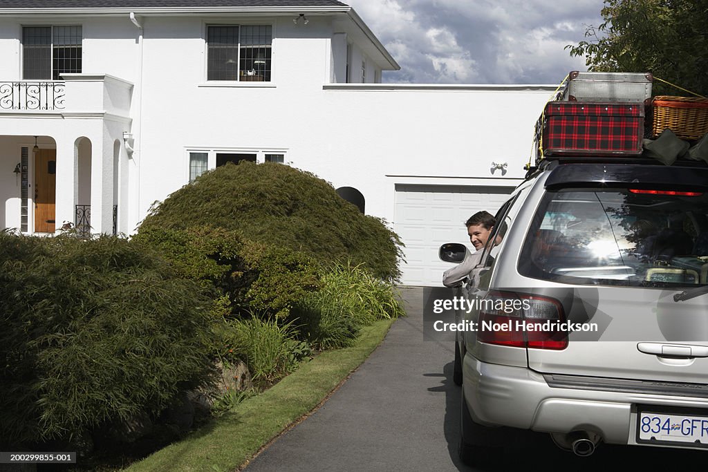 Man looking out of window of car on front drive, smiling