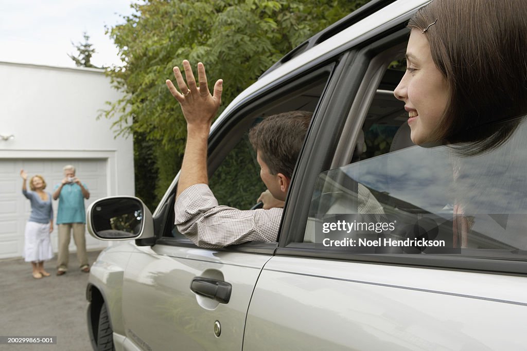 Man and daughter (13-15 years) in car waving to senior couple on drive