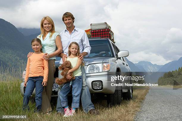 two girls (6-8 years) standing with parents beside car on rural grass verge, portrait - car parked stock pictures, royalty-free photos & images