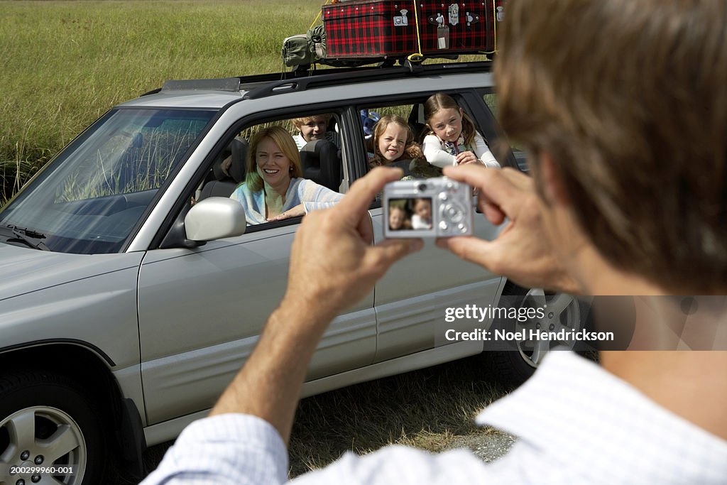 Woman and children (6-8 years) in car being photographed by man, rear view, in foreground