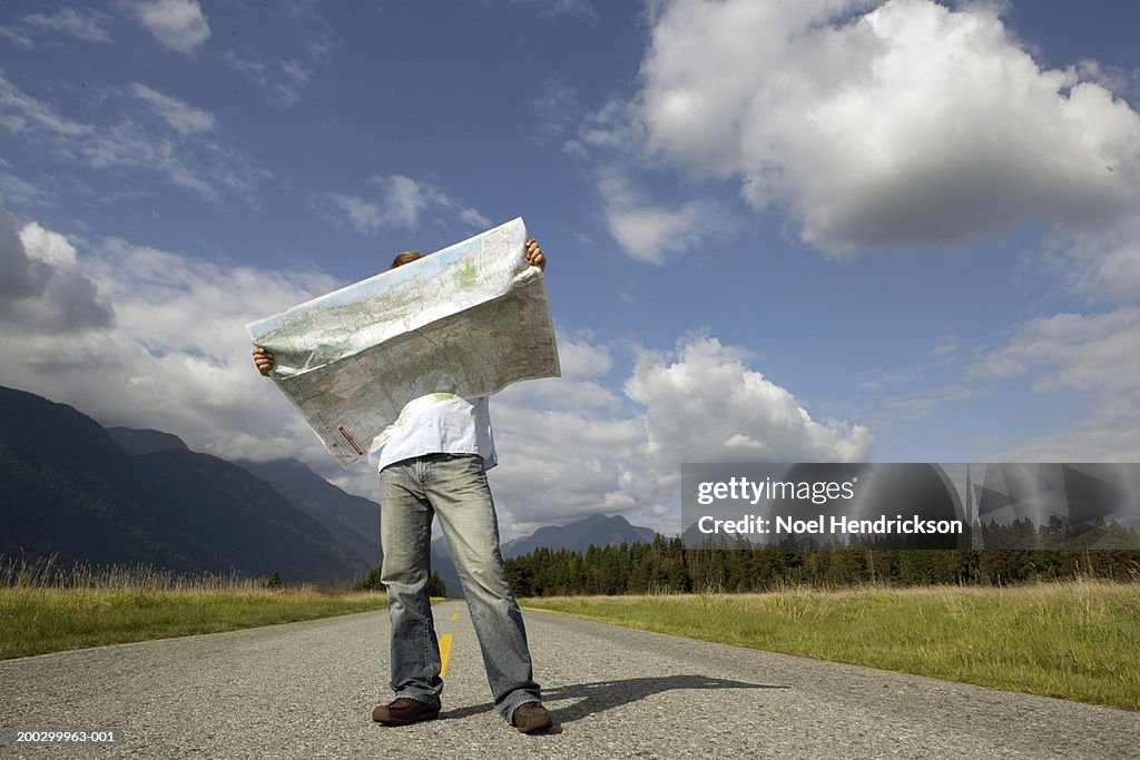 Man standing on rural road holding road map, head obscured by map