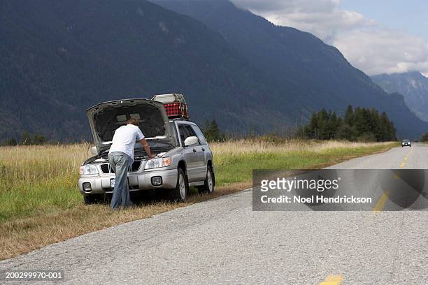 man, rear view, checking engine of sports utility vehicle beside rural road - vehicle breakdown photos et images de collection