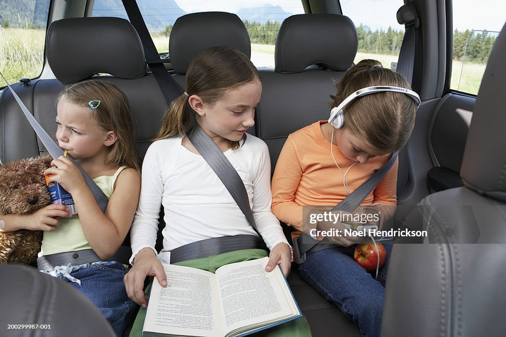 Three girls (6-8 years) sitting on rear seat of car on road trip