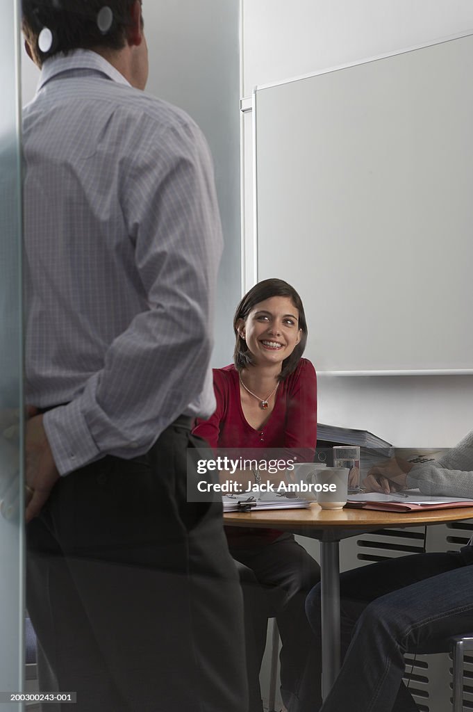 Colleagues in meeting, view through glass, woman in centre smiling