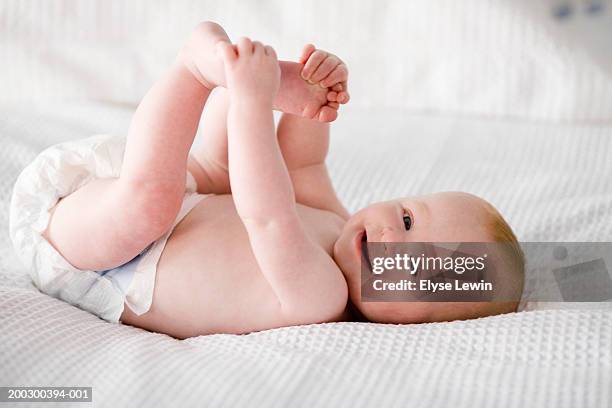 close-up of baby boy (6-9 months) lying on back, holding feet, smiling - diaper stock pictures, royalty-free photos & images