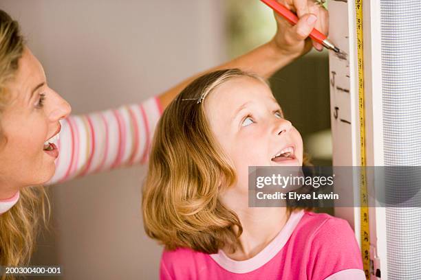 mother measuring girl's (6-8) growth against wall - groeimeter stockfoto's en -beelden