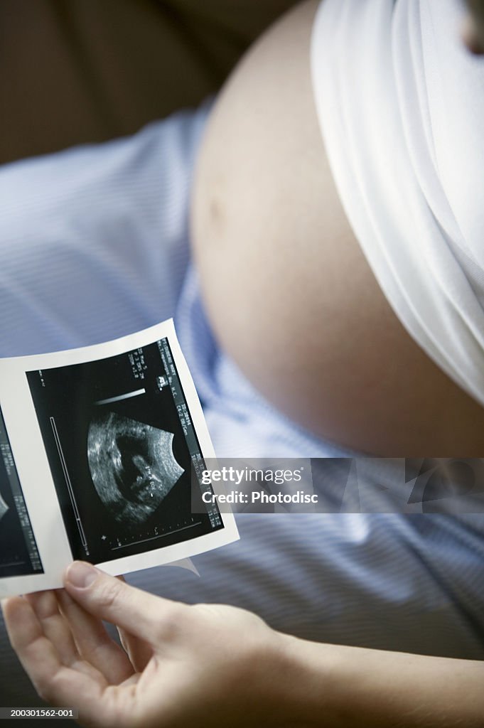 Pregnant woman looking at ultrasound picture, mid section