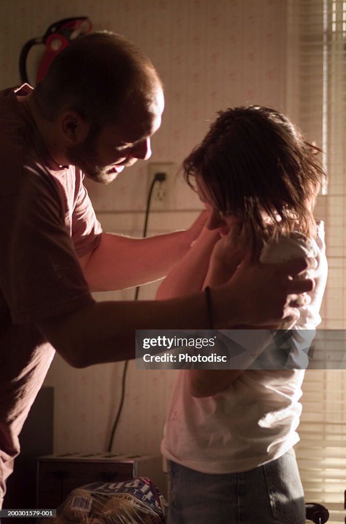 Couple having fight in kitchen, man holding shoulders of woman