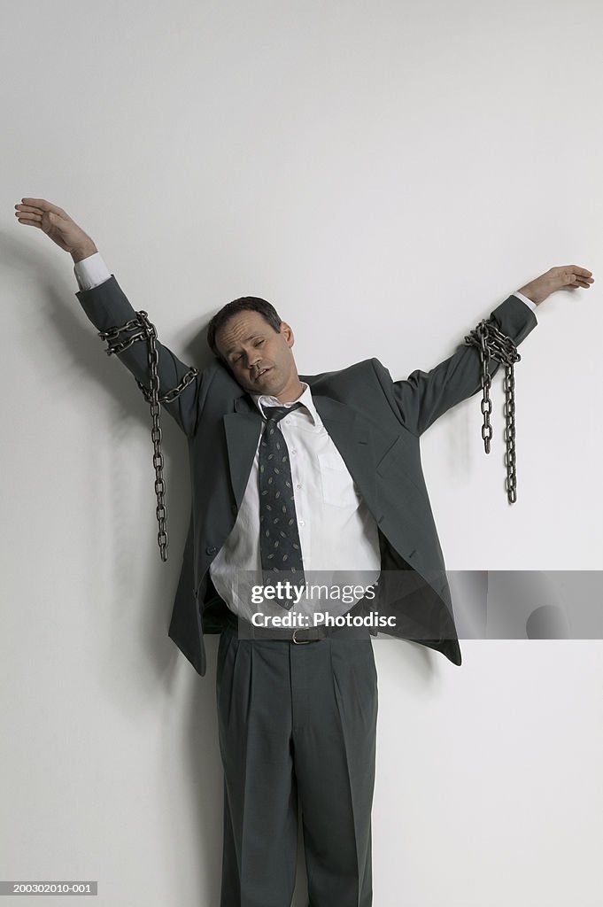 Businessman against wall with chains around arms