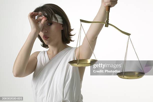 woman dressed as lady justice peeking at scales - lady justice fotografías e imágenes de stock