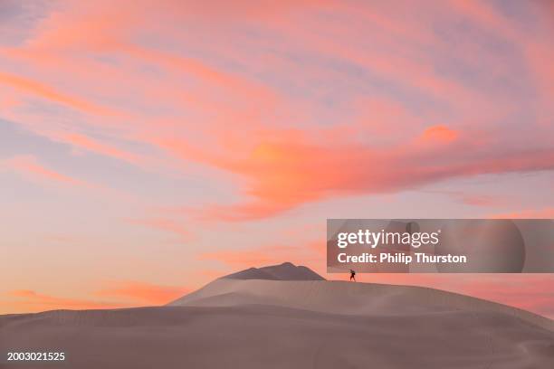 joven mochilero caminando a través de la escena del paisaje árido del desierto con dunas de arena blanca contra un cielo dorado - vida sencilla fotografías e imágenes de stock