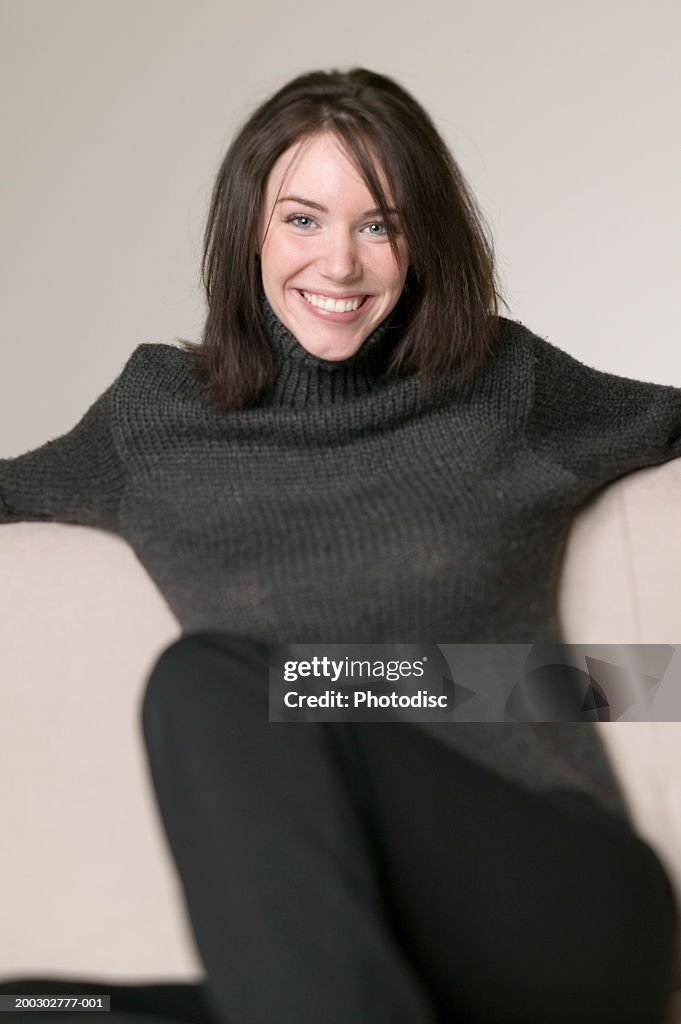 Young woman with dark hair, sitting on sofa, posing in studio, portrait