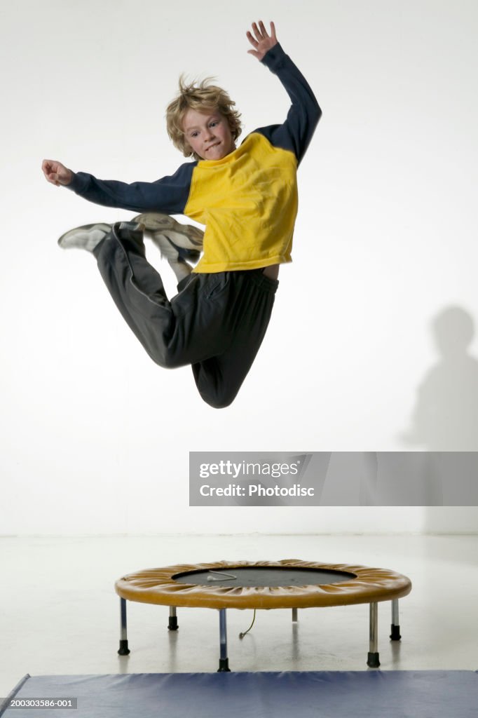 Boy (12-13), jumping on trampoline in studio, portrait