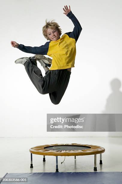 boy (12-13), jumping on trampoline in studio, portrait - boys sport pants stock pictures, royalty-free photos & images